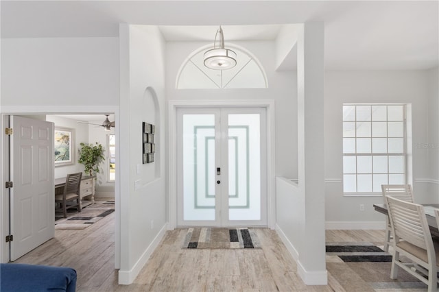 entrance foyer with ceiling fan, light hardwood / wood-style floors, a high ceiling, and french doors