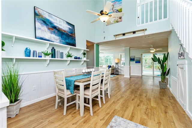 dining space with ceiling fan, light hardwood / wood-style flooring, and a high ceiling