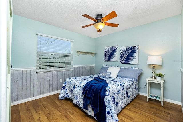 bedroom with ceiling fan, wood-type flooring, wooden walls, and a textured ceiling