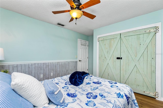 bedroom featuring ceiling fan, hardwood / wood-style floors, a textured ceiling, and wood walls