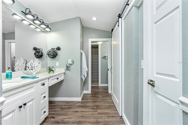 bathroom with hardwood / wood-style flooring, lofted ceiling, vanity, and a textured ceiling