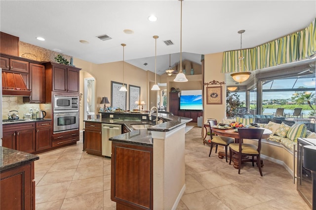 kitchen featuring sink, hanging light fixtures, dark stone counters, a center island with sink, and appliances with stainless steel finishes