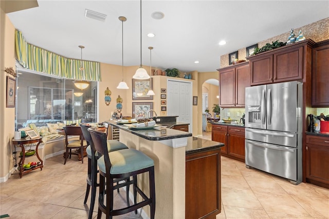 kitchen with hanging light fixtures, stainless steel fridge with ice dispenser, dark stone countertops, a kitchen bar, and light tile patterned floors