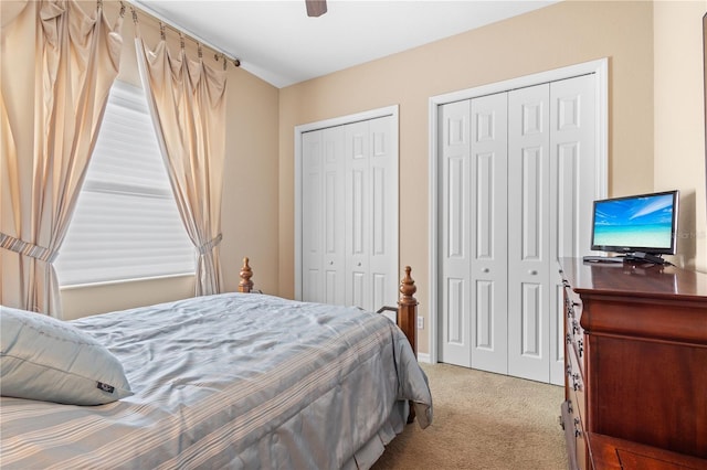 bedroom with light carpet, two closets, and ceiling fan