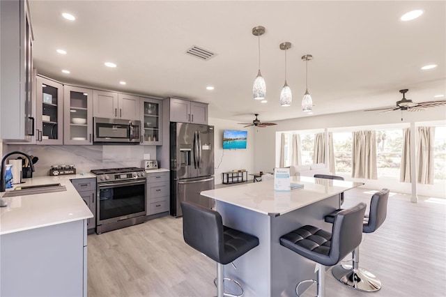 kitchen featuring pendant lighting, gray cabinetry, sink, light wood-type flooring, and appliances with stainless steel finishes