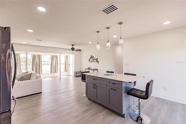 kitchen with hanging light fixtures, a kitchen breakfast bar, light hardwood / wood-style flooring, stainless steel fridge, and gray cabinets