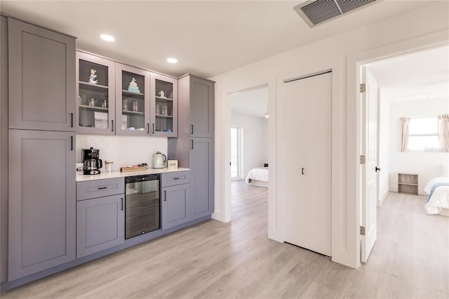 bar with tasteful backsplash, gray cabinets, beverage cooler, and light hardwood / wood-style floors