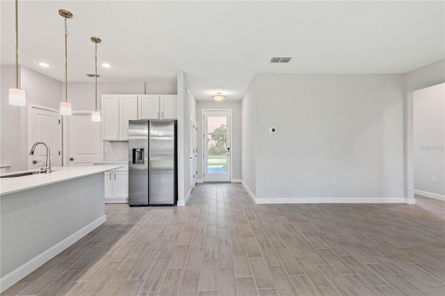 kitchen with sink, white cabinets, pendant lighting, and stainless steel fridge