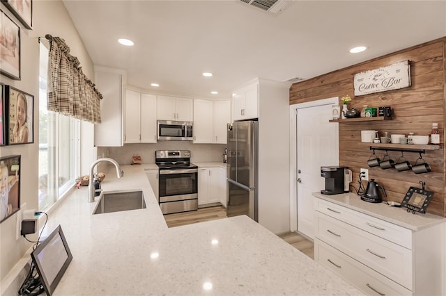 kitchen with light stone countertops, sink, wood walls, white cabinets, and appliances with stainless steel finishes