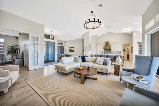 living room with a chandelier, french doors, light wood-type flooring, and high vaulted ceiling