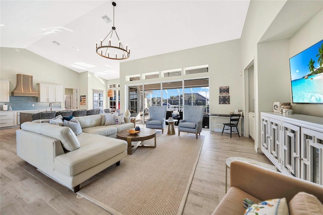 living room with high vaulted ceiling, light wood-type flooring, and an inviting chandelier