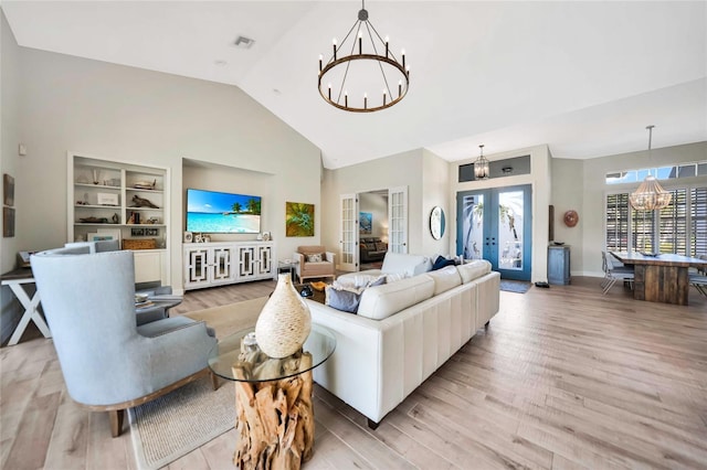 living room featuring french doors, light hardwood / wood-style floors, built in features, and an inviting chandelier