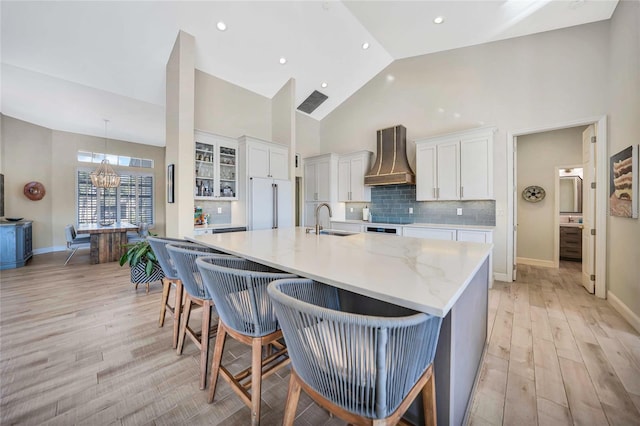 kitchen featuring high vaulted ceiling, sink, custom range hood, white cabinetry, and a chandelier