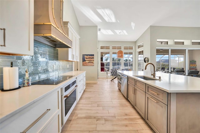 kitchen with backsplash, a kitchen island with sink, sink, light hardwood / wood-style flooring, and appliances with stainless steel finishes