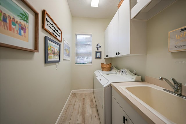 clothes washing area with cabinets, light wood-type flooring, washer and clothes dryer, and sink