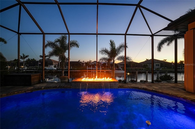 pool at dusk featuring glass enclosure, a water view, pool water feature, and a patio