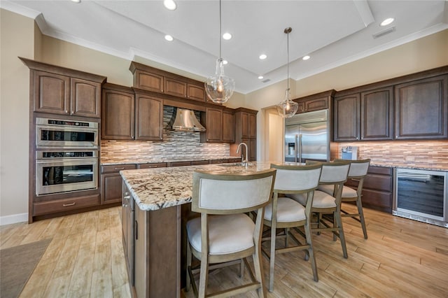 kitchen with wine cooler, a center island with sink, decorative backsplash, hanging light fixtures, and appliances with stainless steel finishes