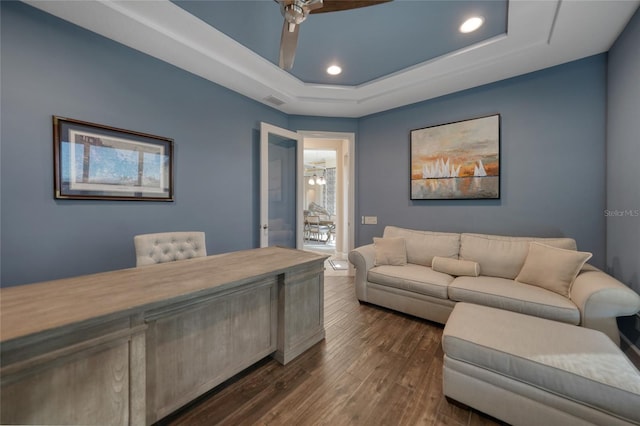 living room with ceiling fan, dark wood-type flooring, and a tray ceiling