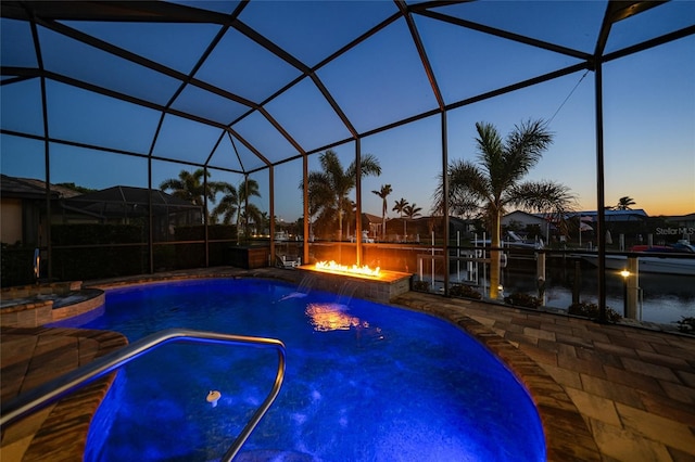 pool at dusk featuring a lanai, pool water feature, a patio, and a fire pit