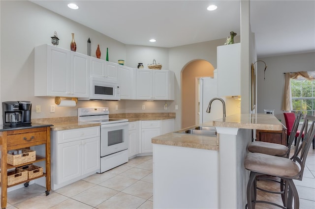 kitchen with sink, light tile patterned floors, white appliances, a breakfast bar area, and white cabinets