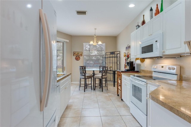 kitchen with pendant lighting, white appliances, an inviting chandelier, light tile patterned floors, and white cabinetry