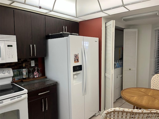 kitchen featuring light tile patterned floors, white appliances, backsplash, dark brown cabinetry, and washer / clothes dryer