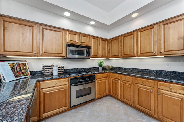 kitchen featuring appliances with stainless steel finishes, light tile patterned flooring, and dark stone countertops