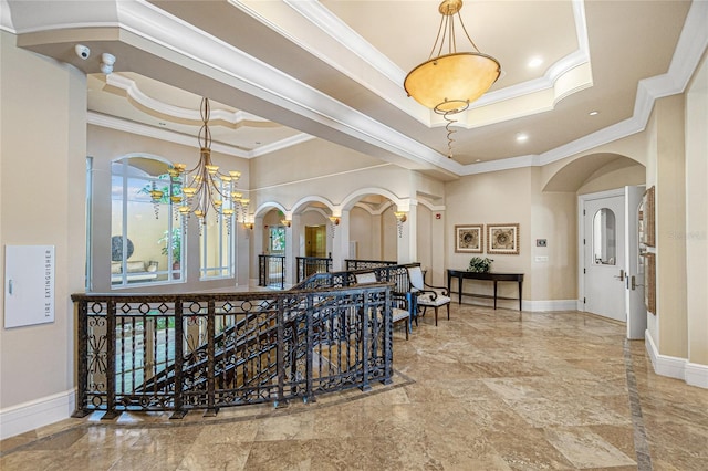 hallway featuring ornamental molding, a notable chandelier, a raised ceiling, and a wealth of natural light