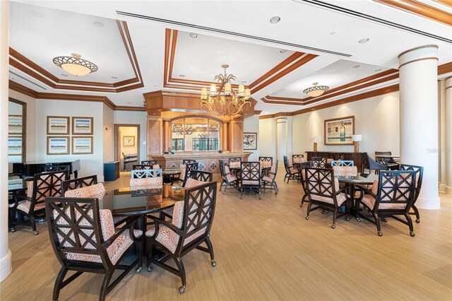 dining room with decorative columns, a chandelier, a raised ceiling, crown molding, and light wood-type flooring