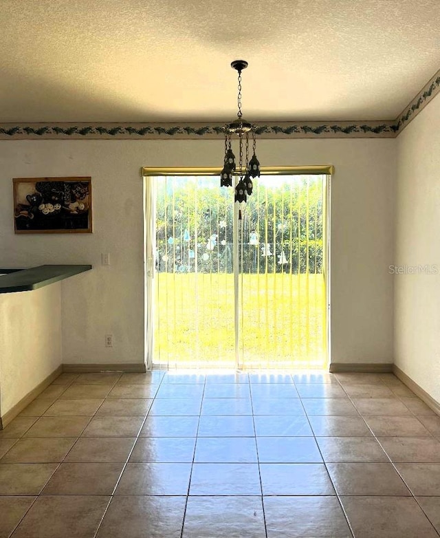 unfurnished dining area featuring a textured ceiling, plenty of natural light, baseboards, and tile patterned floors