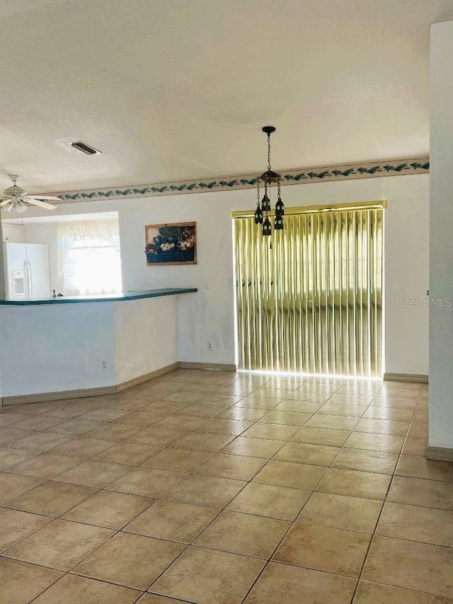 spare room featuring a textured ceiling, ceiling fan, light tile patterned floors, visible vents, and baseboards