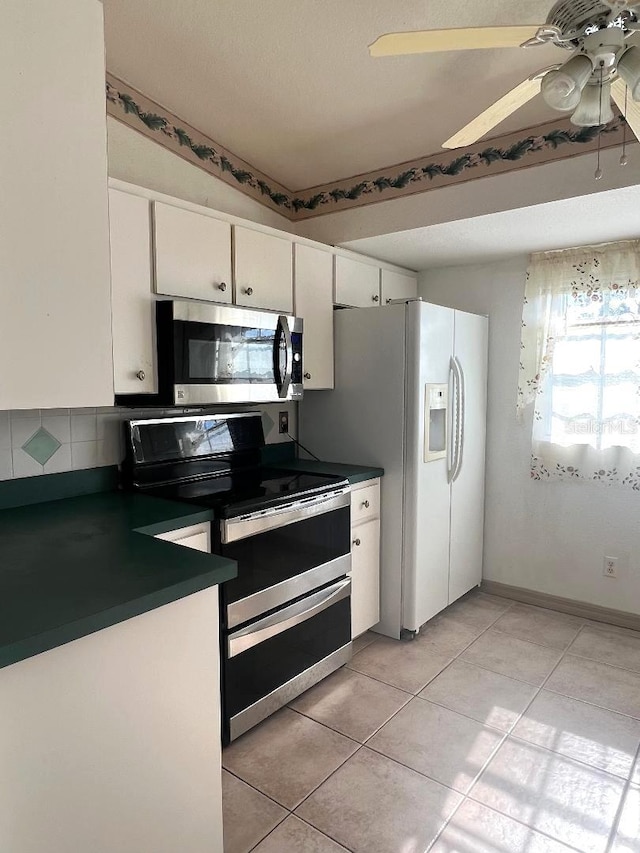 kitchen featuring light tile patterned floors, white cabinetry, a ceiling fan, appliances with stainless steel finishes, and dark countertops