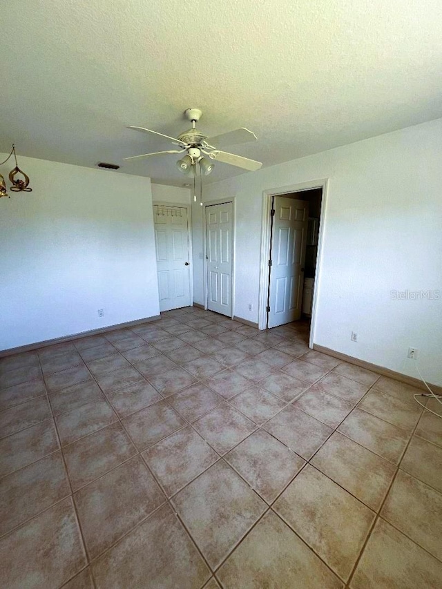 empty room featuring ceiling fan, a textured ceiling, light tile patterned flooring, visible vents, and baseboards