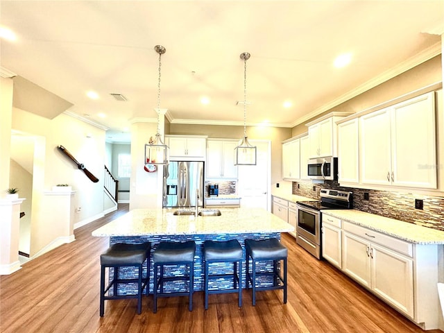 kitchen with sink, light hardwood / wood-style flooring, pendant lighting, a kitchen island with sink, and appliances with stainless steel finishes