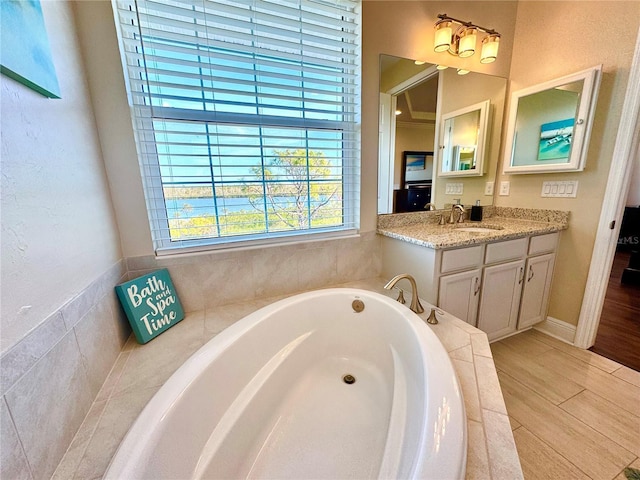 bathroom featuring wood-type flooring, vanity, and a relaxing tiled tub