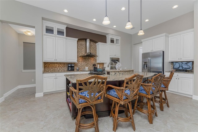 kitchen with light stone countertops, white cabinetry, a kitchen island with sink, and wall chimney range hood