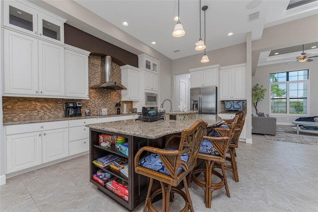 kitchen featuring backsplash, wall chimney range hood, a center island with sink, appliances with stainless steel finishes, and white cabinets