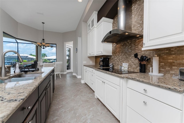 kitchen featuring black electric cooktop, wall chimney range hood, a chandelier, white cabinets, and sink