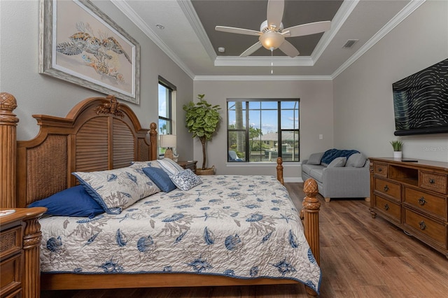 bedroom with ceiling fan, ornamental molding, wood-type flooring, and a raised ceiling