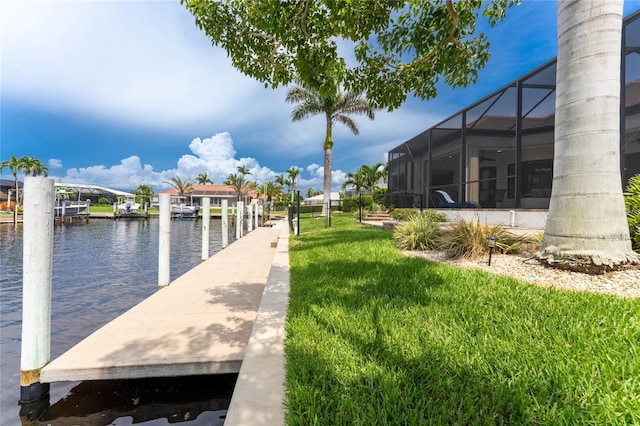 view of dock with a water view, a lawn, and glass enclosure