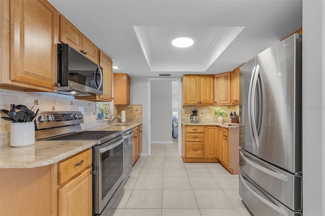 kitchen featuring light tile patterned floors, a tray ceiling, tasteful backsplash, light stone counters, and stainless steel appliances