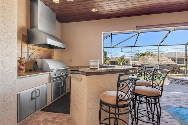 kitchen featuring a breakfast bar, wall chimney range hood, kitchen peninsula, and wooden ceiling