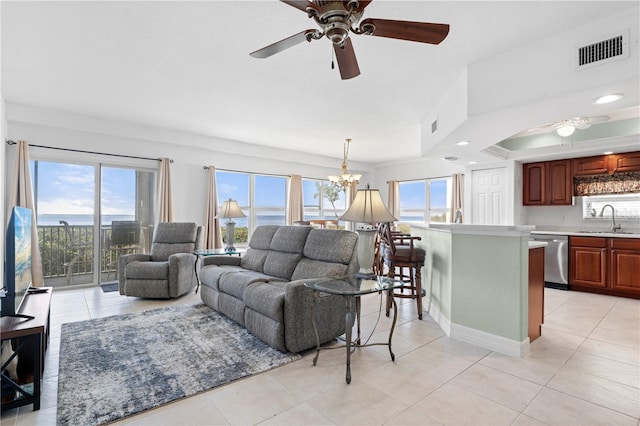 living room featuring ceiling fan with notable chandelier, a water view, sink, light tile patterned floors, and a tray ceiling