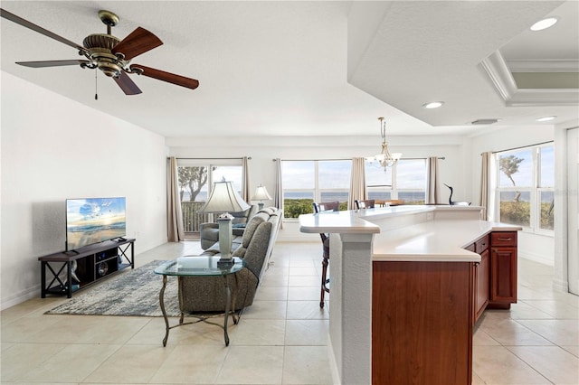 kitchen featuring a center island, decorative light fixtures, a tray ceiling, ceiling fan with notable chandelier, and ornamental molding