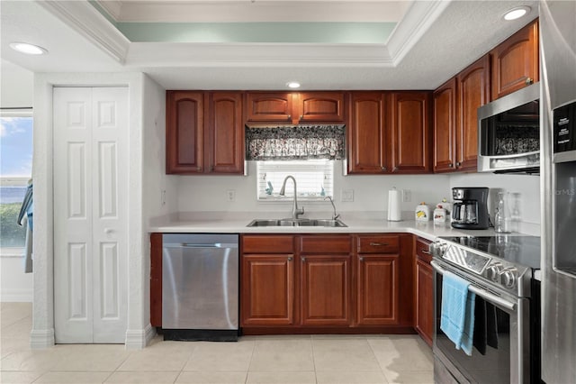 kitchen with ornamental molding, stainless steel appliances, a tray ceiling, sink, and light tile patterned floors