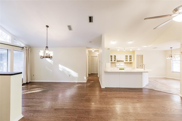 unfurnished living room with ceiling fan with notable chandelier, sink, dark wood-type flooring, and vaulted ceiling