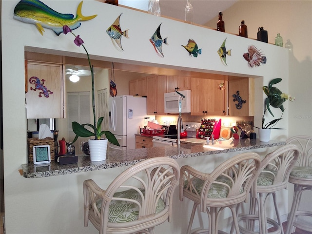 kitchen with white appliances, stone counters, kitchen peninsula, and light brown cabinets