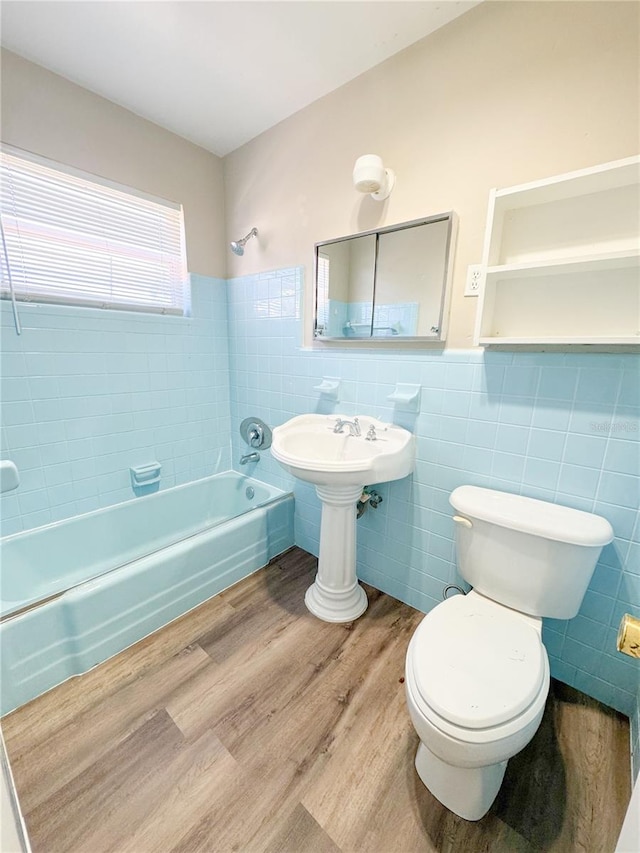 bathroom featuring hardwood / wood-style floors, tiled shower / bath combo, toilet, and tile walls