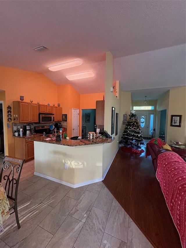 kitchen with kitchen peninsula, appliances with stainless steel finishes, a textured ceiling, and vaulted ceiling