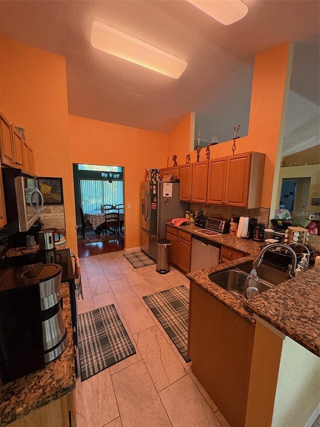 kitchen with appliances with stainless steel finishes, dark stone countertops, sink, kitchen peninsula, and vaulted ceiling